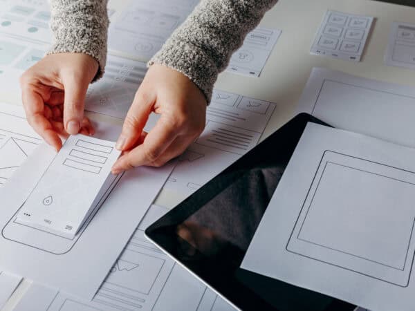 Hände platzieren Papierprototypen auf einem Tisch mit Layouts.