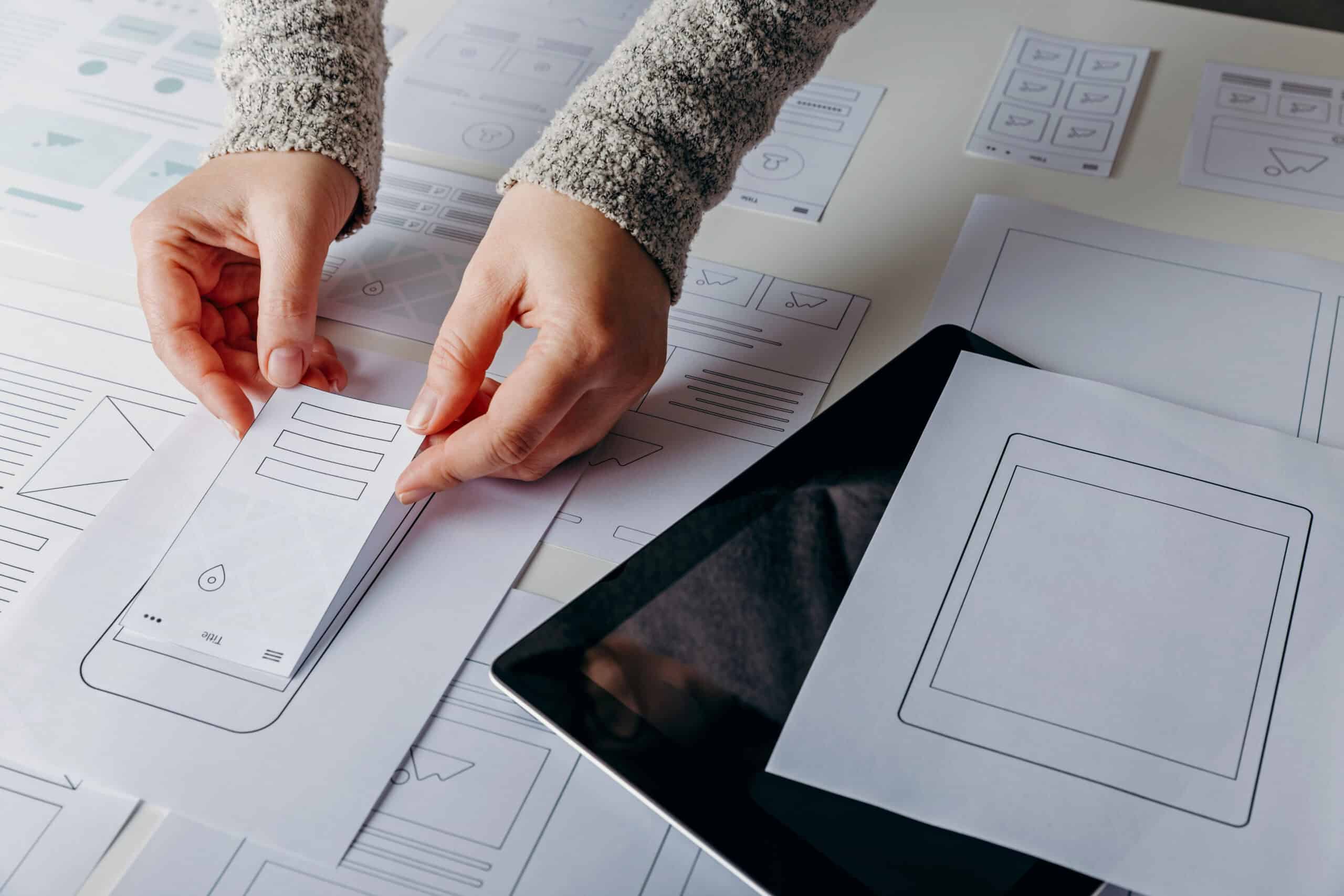 Hände platzieren Papierprototypen auf einem Tisch mit Layouts.