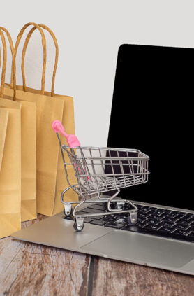 Online Einkaufen mit Einkaufstüten und Laptop Einkaufswagen auf einem Laptop mit Papiertüten im Hintergrund.