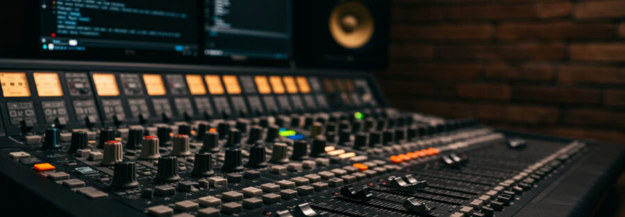 Nahaufnahme einer Audiomischkonsole mit Reglern und Monitoren.