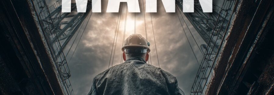 Mann in industrieller Umgebung mit Helm und dunklem Anzug.